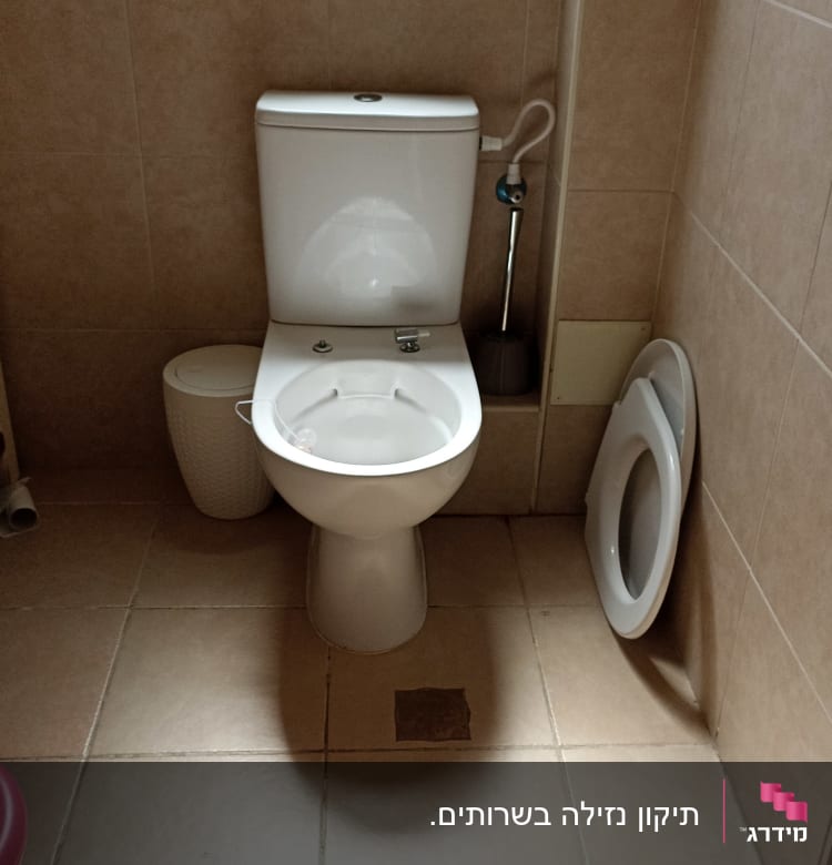 אסלה עם מברשת ניקוי ומכסה מונח בצד